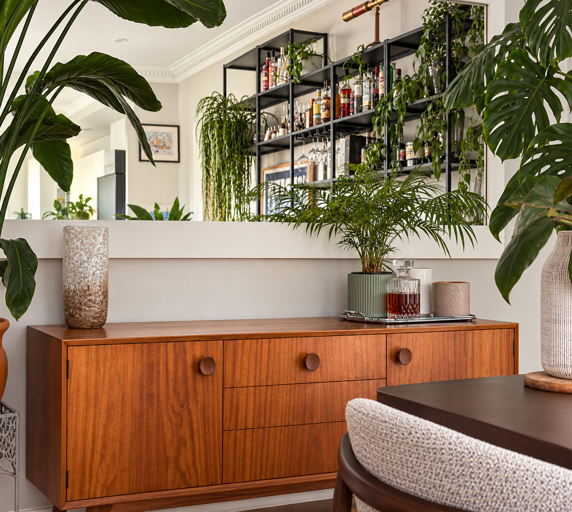 Interior detail with a walnut sideboard, broad mirror, layered greenery and glassware.